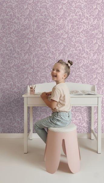 Ein Mädchen sitzt an einem Schreibtisch vor einer floralen Tapete.