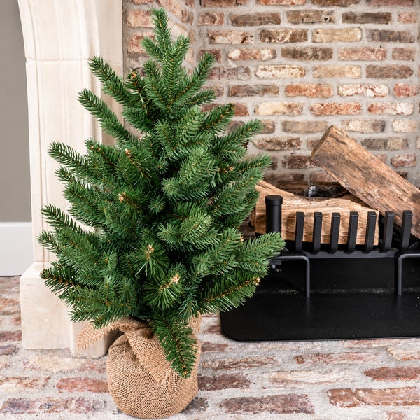 Künstlicher Weihnachtsbaum in Jutesack vor einem Kamin aus Ziegelsteinen