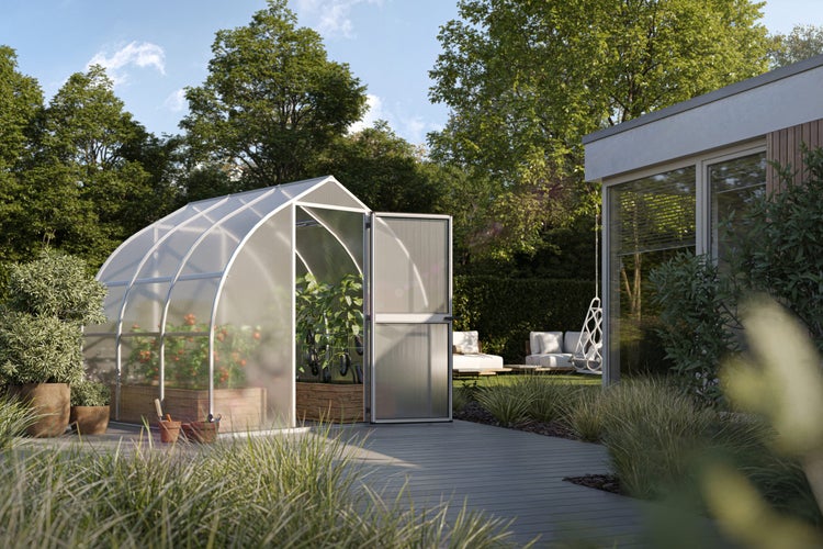 Modernes Gewächshaus mit gebogenem Dach in einem hellen Garten, bepflanzt mit Tomaten in Hochbeeten, neben einer Holzterrasse.