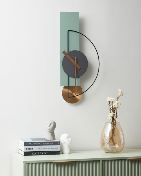 Moderne Wanduhr mit abstrakten geometrischen Formen über einem Sideboard mit Büchern, Kopfskulpturen und einer Blumenvase.