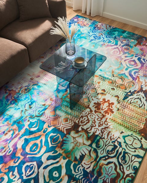Moderner Wohnbereich mit buntem Teppich in Patchwork-Optik, braunem Sofa und gläsernem Couchtisch.