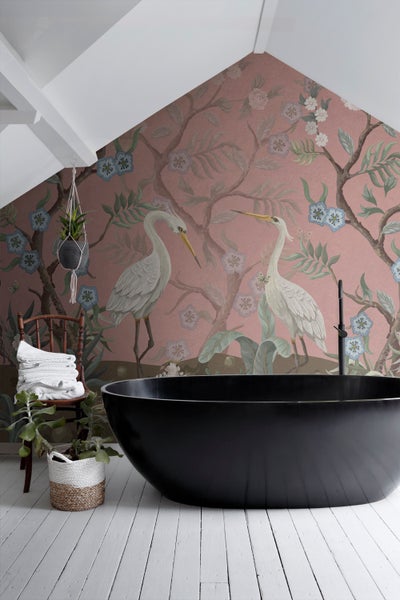 Badezimmer mit freistehender Badewanne, Stuhl mit Handtüchern und floraler Tapete mit Reihermotiven