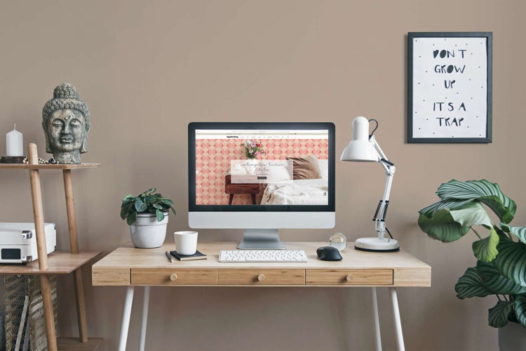 Hell eingerichteter Arbeitsplatz mit Holzschreibtisch, Computer, Schreibtischlampe und Zimmerpflanzen. Monitor zeigt gemusterte Tapete.