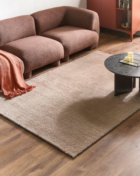 Strukturierter rechteckiger Teppich in einem modernen Wohnzimmer mit einem braunen Bouclé-Sofa, schwarzem Couchtisch und Boden in Holzoptik.