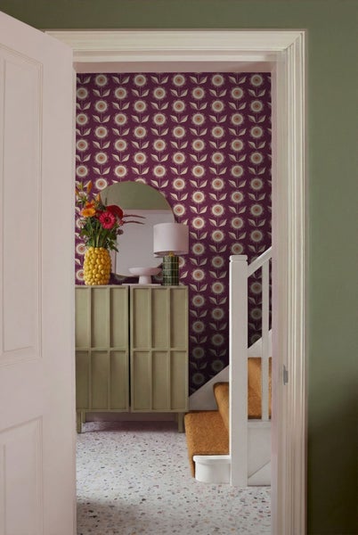 Blick durch eine Tür in einen Flur mit Blumendekor, Kommode, Spiegel und Treppe.