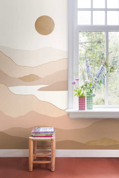 Heller Raum mit Wandbild eines Bergpanoramas und einem kleinen Holzhocker mit Büchern