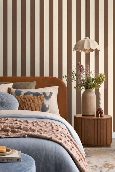Stilvolles Schlafzimmer mit gestreifter Tapete, Bett mit gepolstertem Kopfteil, Nachttisch aus Holz und dekorativer Pendelleuchte.