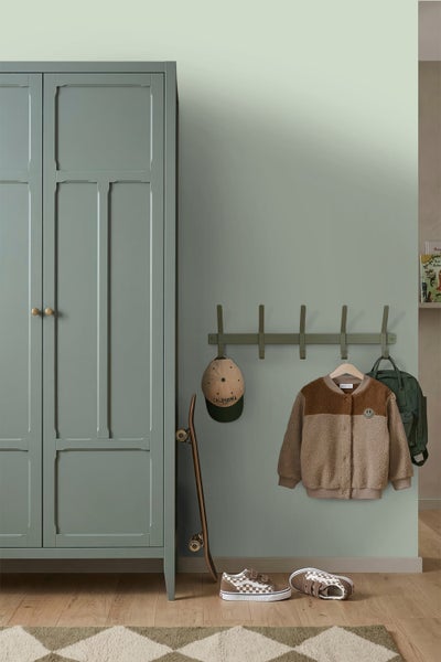 Organisiertes Zimmer mit grünem Kleiderschrank, Hakenleiste mit Jacke, Rucksack und Kappe, Skateboard und Sneakern auf Holzboden.