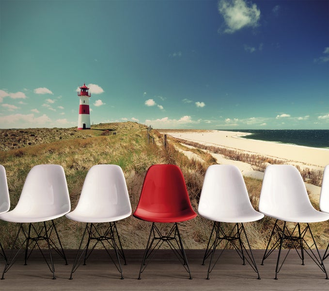 Fototapete mit Küstenmotiv aus Leuchtturm, Dünen und Strand, davor eine Reihe moderner Schalenstühle in einem hellen Raum.