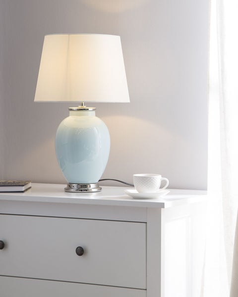 Dekorative Tischleuchte auf einem Nachttisch mit Schubladen und einer Tasse.