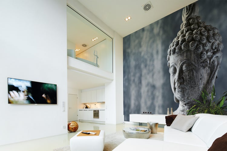 Modernes, helles Wohnzimmer mit einer großflächigen Fototapete eines Buddha-Kopfes, weißem Sofa und offener Küche im Hintergrund.