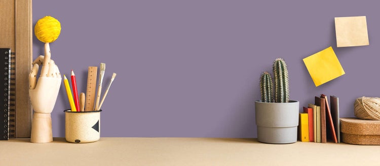 Schreibtisch mit Holzhand und Kugel, Becher mit Stiften, Lineal und Pinseln, Kaktus im Topf, Büchern, Notizzetteln und Korkbehältern.