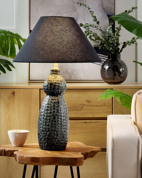 Dekorative Tischleuchte mit gemustertem Keramikfuß und Stoffschirm auf einem Holztisch