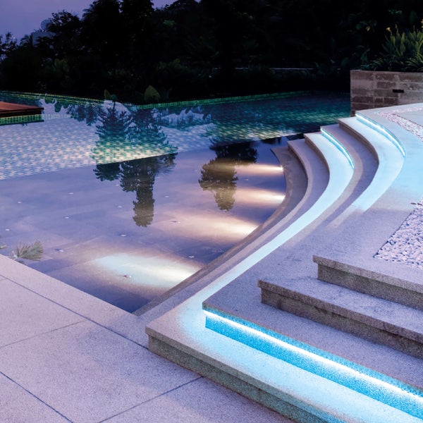 Beleuchteter Pool mit Steintreppe und Kieselsteinen im Garten