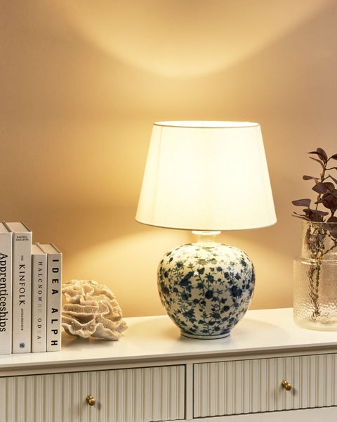 Dekorative Tischleuchte mit Blumenmuster und Lampenschirm auf einer Kommode mit Büchern, Koralle und einer Vase