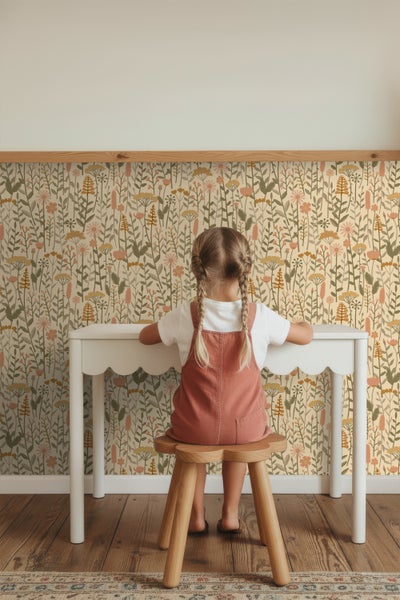 Mädchen sitzt an einem weißen Kinderschreibtisch vor einer floralen Tapete