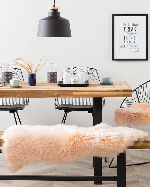 Hell gestalteter Essbereich mit Massivholztisch, schwarzen Metallstühlen und einer Sitzbank mit flauschigem pfirsichfarbenem Kunstfellüberzug.