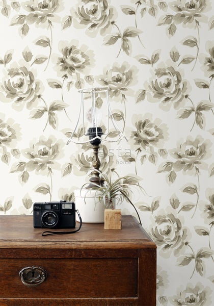 Szene mit einer Kommode, einer Lampe, einer Zimmerpflanze und einer Kamera vor einer floralen Tapete