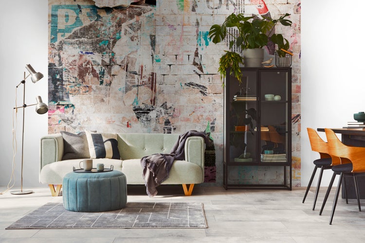 Modernes Wohnzimmer mit hellgrünem Sofa, blauem Hocker, schwarzer Vitrine und einer Fototapete im urbanen Backstein-Design.