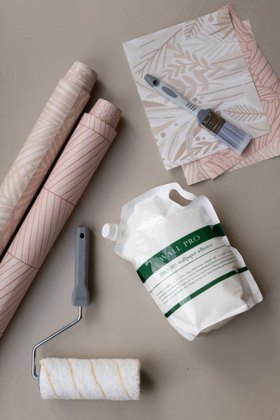 Tapetenzubehör-Set bestehend aus zwei gemusterten Tapetenrollen, einem Beutel Tapetenkleister, einer Malerwalze und einem Pinsel.