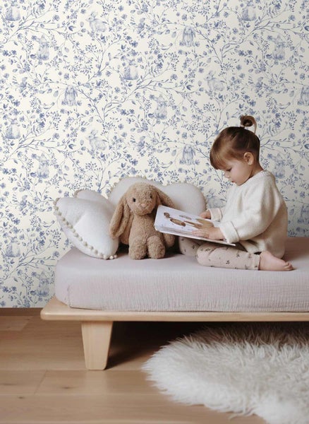Tapete mit floralem Muster und Hasenmotiven in einem hellen Kinderzimmer mit einem Kind auf einem Bett.