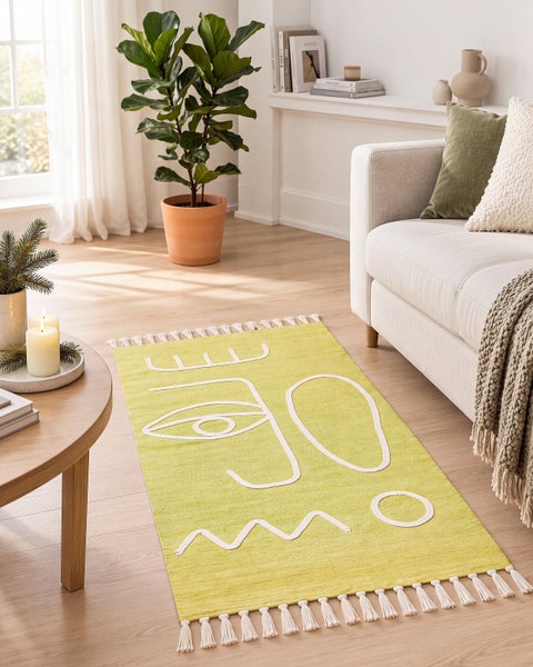 Moderner Webteppich mit abstraktem Gesichtsmotiv und Fransen in einem hellen Wohnzimmer vor einem Sofa.