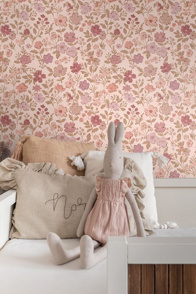 Tapete mit Blumenmuster in einem hellen Kinderzimmer mit einem Kinderbett, Kissen und einem Stoffhasen.