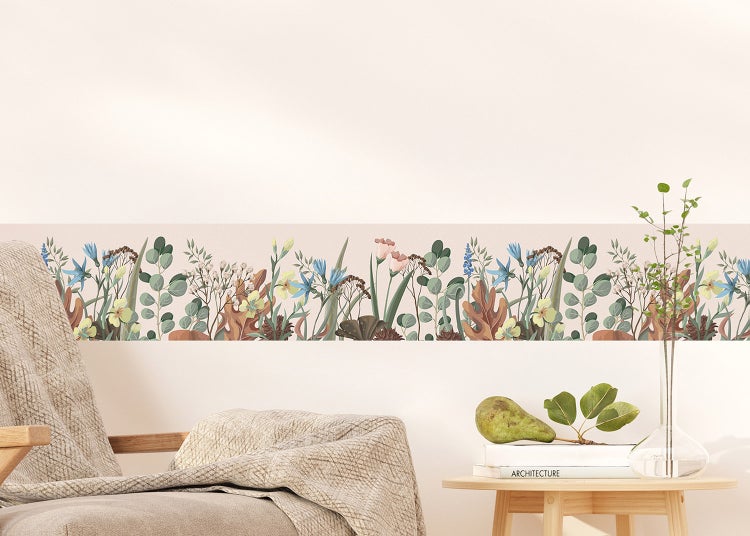 Selbstklebende Tapetenbordüre mit Wiesenblumen-Motiv an einer hellen Wand über einem Sessel und Beistelltisch.