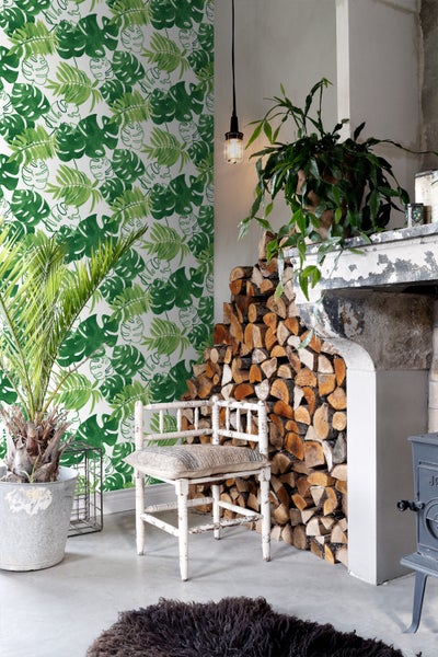 Wohnzimmer mit gemusterter Tapete, Kamin mit Holzscheiten und Pflanzen