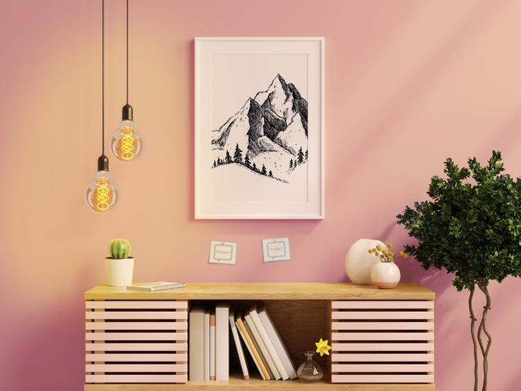 Dekoratives Interieur mit Holzkommode, Lampe, Topfpflanze und gerahmtem Bergmotiv