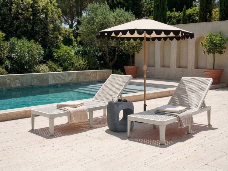 Poolszene mit Sonnenliegen, einem Beistelltisch und einem Sonnenschirm mit Bogenrand neben einem Schwimmbecken und einer Steinmauer.