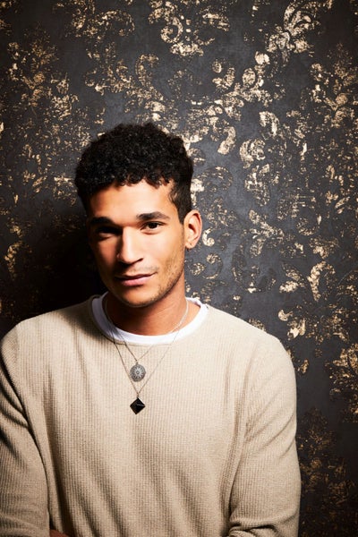 Porträt eines Mannes mit Pullover und Halsketten vor einer verzierten Wand