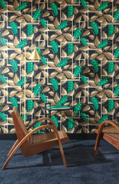 Raumansicht mit gemusterter Tapete, Stehlampe, kleinem Tisch und zwei Holzstühlen.