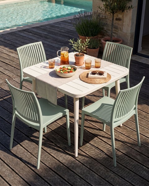 Modernes Gartenmöbel-Set mit weißem quadratischem Tisch und vier mintgrünen Stühlen auf einer Holzterrasse am Pool.