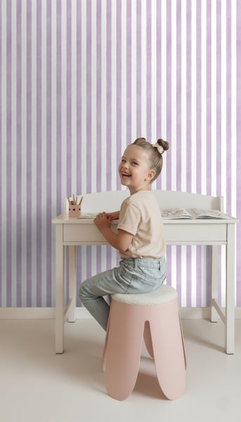Kind sitzt an einem Schreibtisch vor einer Wand mit Streifentapete.