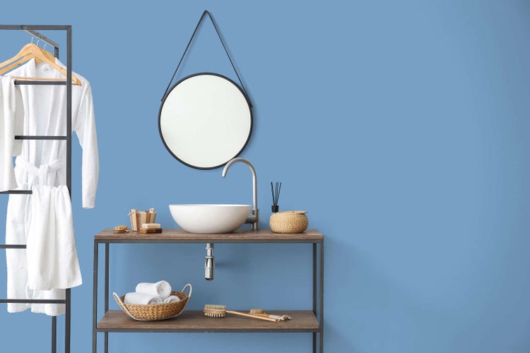 Organisiertes, helles Badezimmer im modernen Stil mit Aufsatzwaschbecken auf einem Holzregal, rundem Wandspiegel und Badezimmerzubehör.