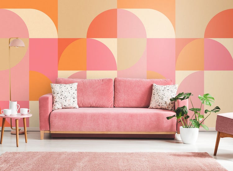 Wohnzimmer mit Sofa, Teppich, Tisch und Zimmerpflanze vor einer geometrischen Tapete.