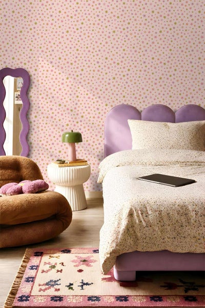 Ein Kinderzimmer mit Tapete mit Sternenmuster, einem Polsterbett, einem wellenförmigen Wandspiegel, einem Beistelltisch und einem Teppich.