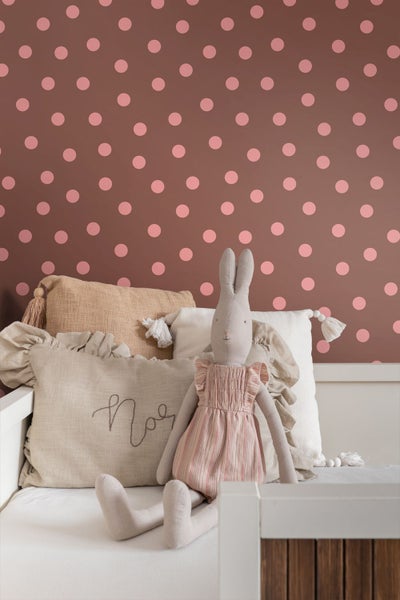 Vliestapete mit Punktemuster in einem Kinderzimmer hinter einem Bett mit verschiedenen Kissen und einem Hasen-Stofftier.