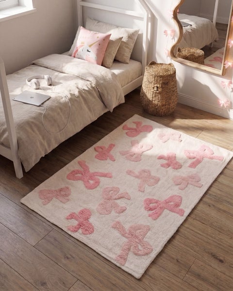 Kinderzimmer mit weißem Hausbett, flauschigem Teppich mit Schleifenmuster und geflochtenem Aufbewahrungskorb auf Holzboden.