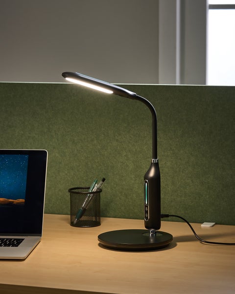 Moderne schwarze LED-Schreibtischlampe mit flexiblem Hals und integriertem Display auf einem Schreibtisch neben einem Laptop.
