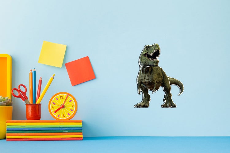 Wandtattoo eines Tyrannosaurus Rex in einem Kinderzimmer über einem Schreibtisch mit Stiften, Heften und einer Uhr.