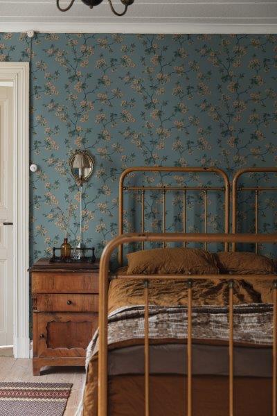 Schlafzimmer mit floraler Tapete, Bettgestell aus Metall und Holzkommode