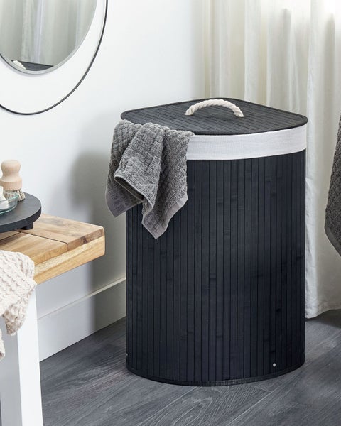 Wäschekorb aus dunklem Bambus mit Deckel, Seilgriff und hellem Wäschesack in einem hellen Badezimmer neben einer Holzbank.