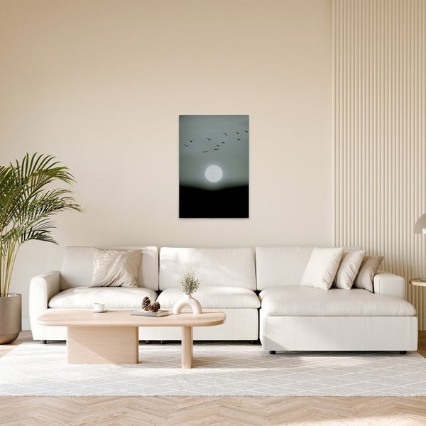 Wohnzimmer mit Sofa, Tisch und einem gerahmten Bild an der Wand, das eine stilisierte Szene mit Vögeln vor einem Vollmond zeigt.