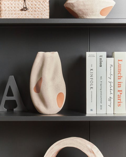 Dekorative Gegenstände auf einem Regal, darunter eine Vase, Bücher und ein Korb