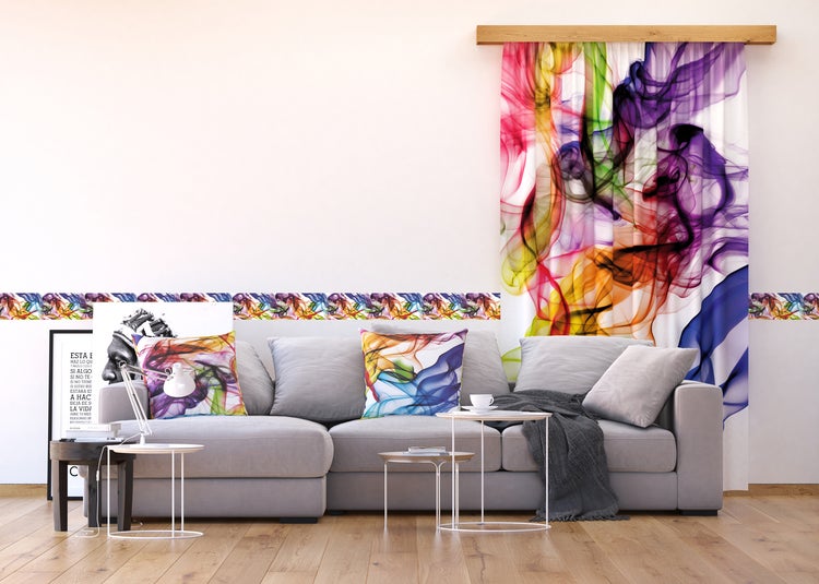 Wohnzimmer mit grauer Couch, dekorativen Kissen, farbenfroher Bordüre und Vorhang mit Rauchmuster