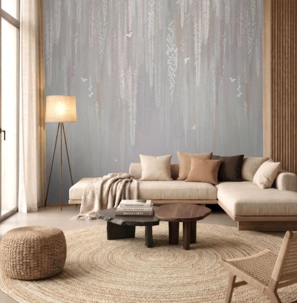 Wohnzimmer mit Fototapete mit hängenden Weidenzweigen und Schmetterlingen, helles Ecksofa, runder Jute-Teppich, hölzerne Couchtische und Stehlampe.