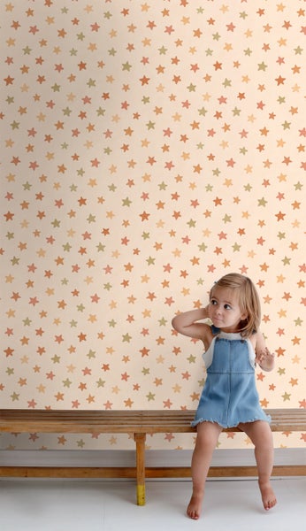 Mädchen sitzt vor einer Wand mit Sternentapete auf einer Holzbank.