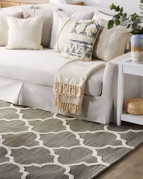 Wohnzimmer-Szene mit Sofa, Kissen, Decke und gemustertem Teppich